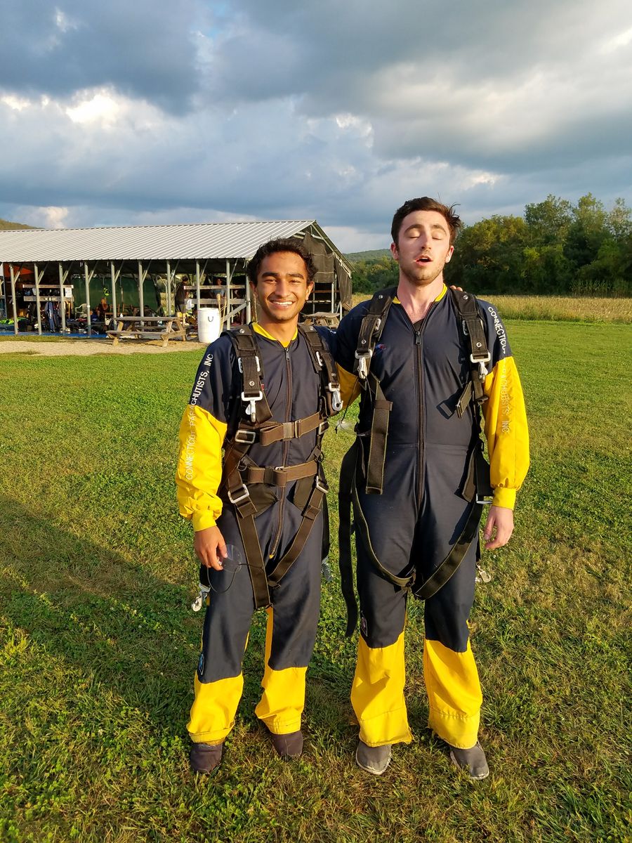 Mufaddal and a friend in skydiving jumpsuits on a grassy airfield