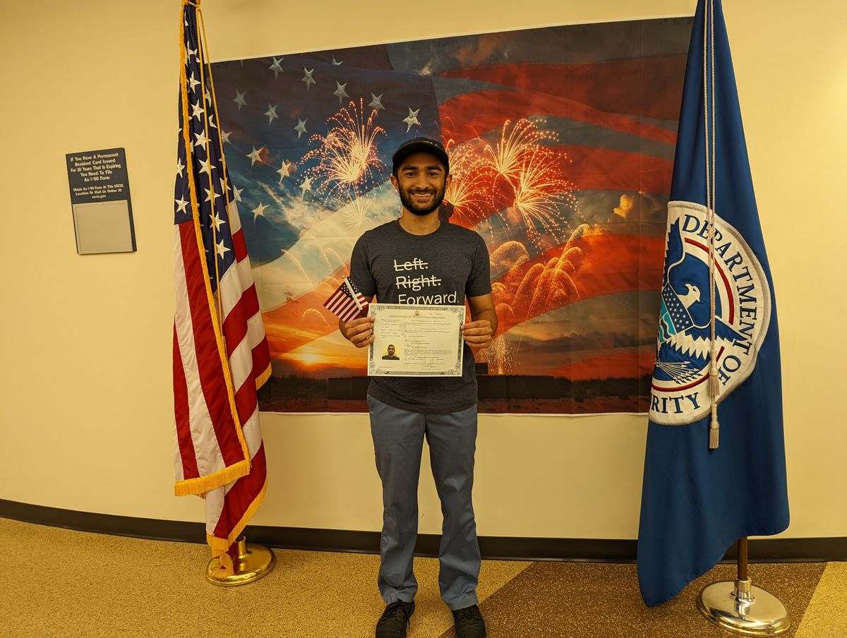 Mufaddal holding his US naturalization certificate in front of US flags