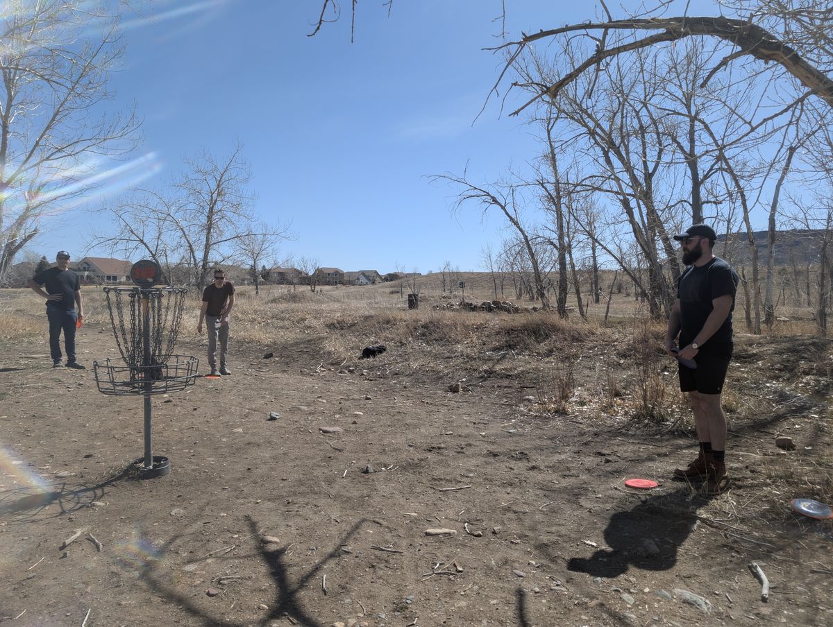 Three men playing disc golf by a reservoir